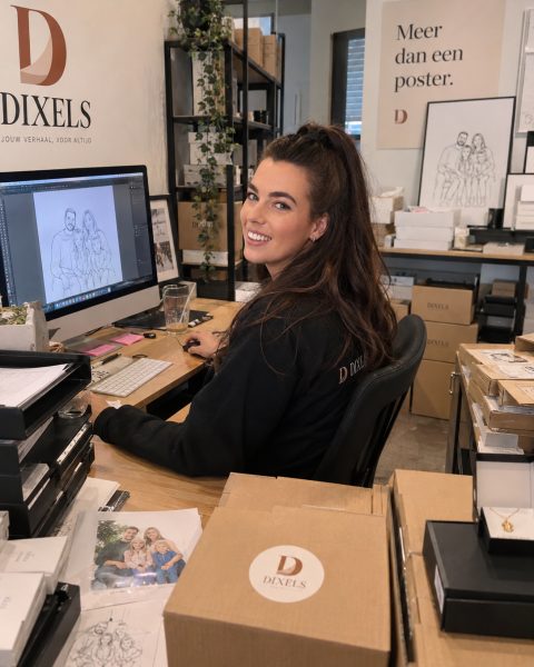 Candy achter haar bureau, met een tekening op het scherm, kijkt om naar de camera